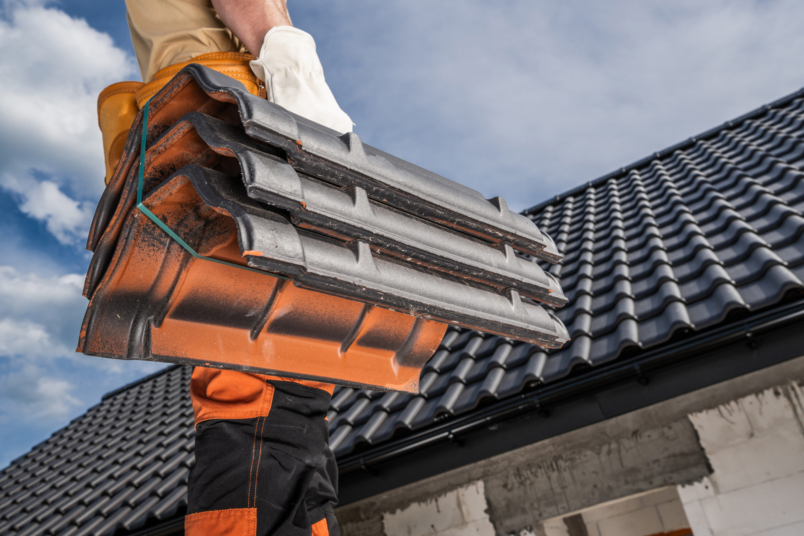 Caucasian construction roofer worker is standing on a roof, holding ceramic roof tiles.