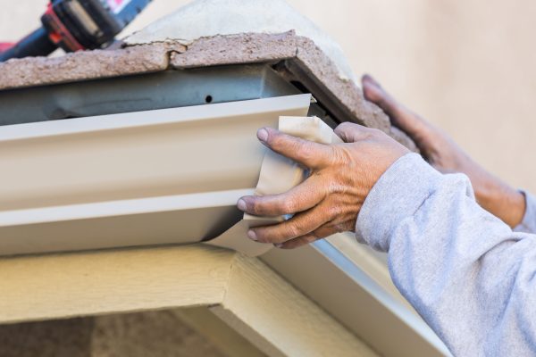 Worker Attaching Aluminum Rain Gutter to Fascia of House.